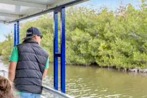 Guest in a vest standing on the Cocoa Beach Eco Tours pontoon boat beside the mangroves