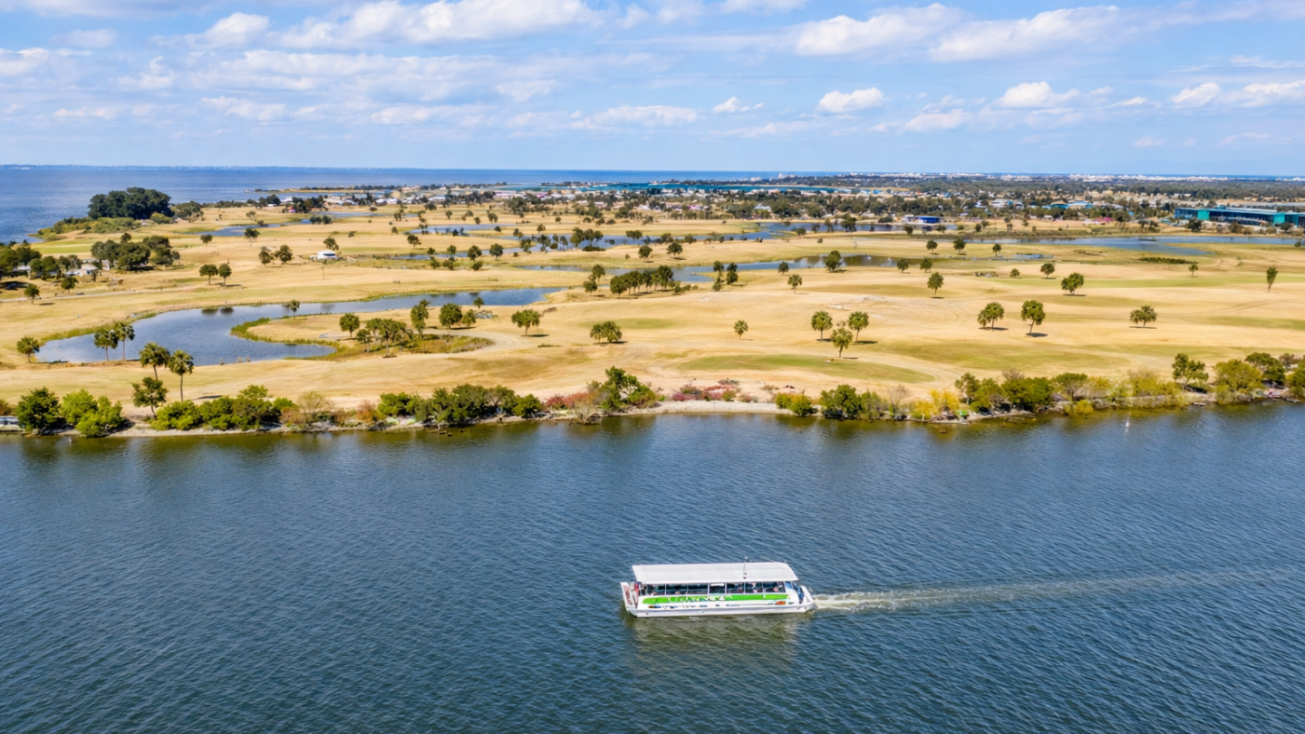 Aerial view of a boat on a river, with a golf course in the background.
