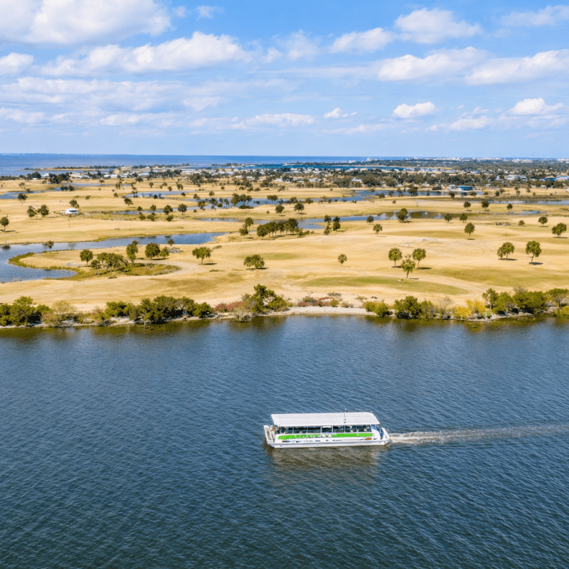 Aerial view of a boat on a river, with a golf course in the background.