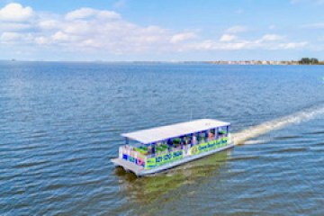 A colorful boat cruises on a calm lake under a partly cloudy sky.