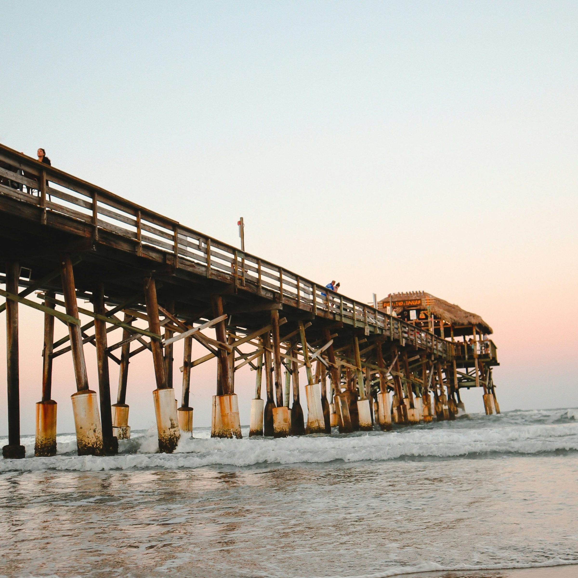 Wooden pier over ocean at sunset, reflections on wet sand.