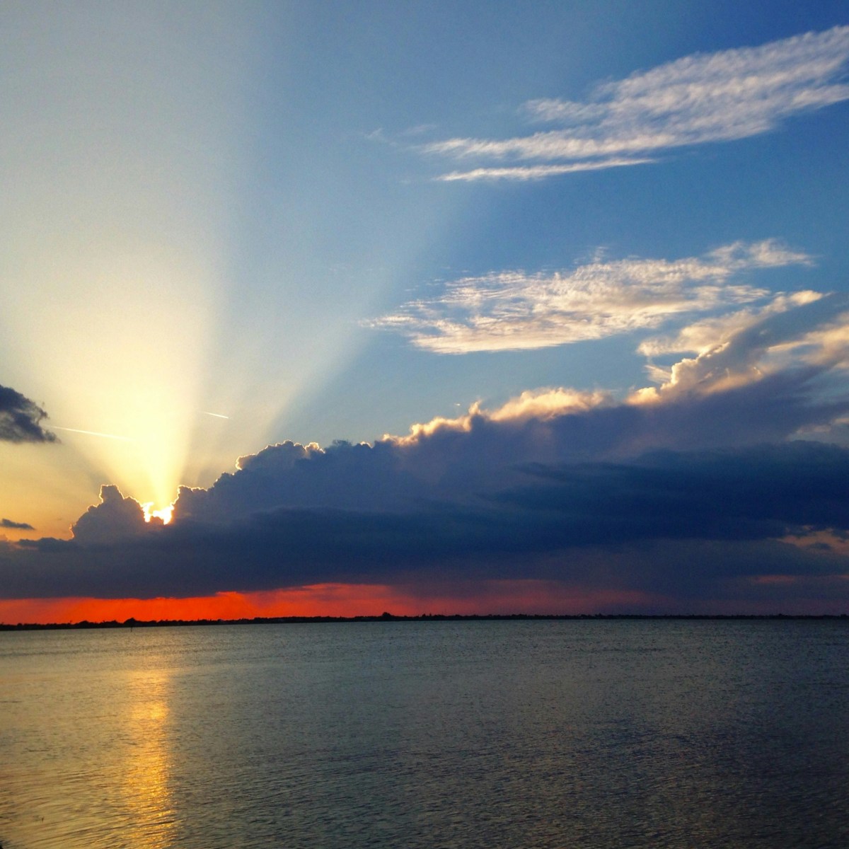 Sunset over a calm lake with sun rays through clouds, reflecting on water.