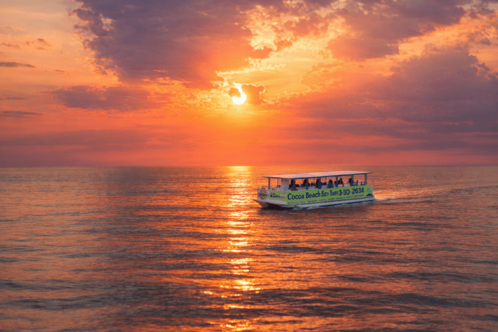 Boat on ocean at sunset with vibrant orange sky and scattered clouds.